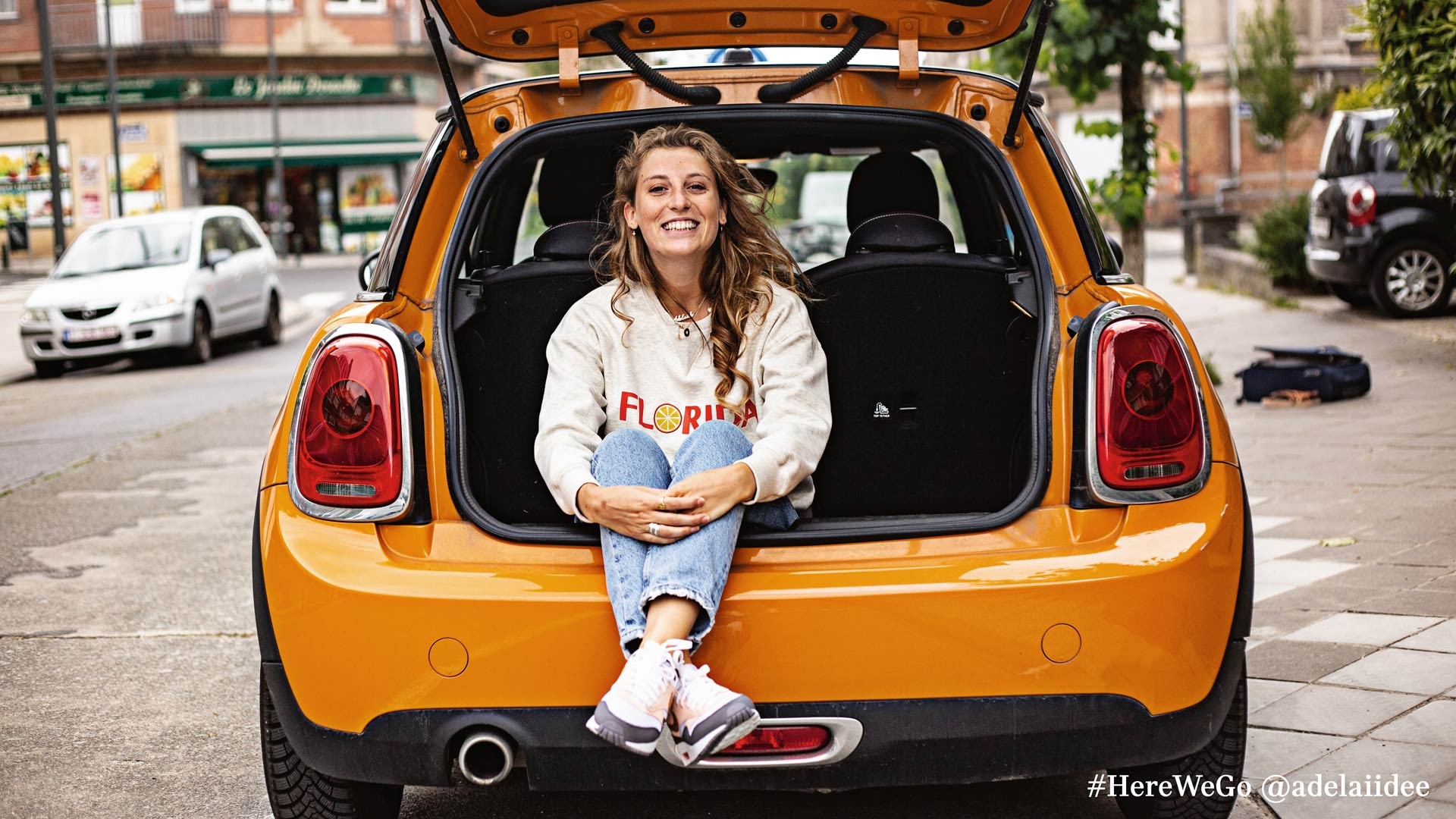 MINI 3-Türer Hatch in Volcanic Orange mit glücklicher Frau, die im Kofferraum sitzt